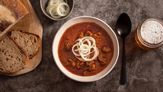 Mísa s chilli kon carne, nakrájená cibule a kousky chleba.
