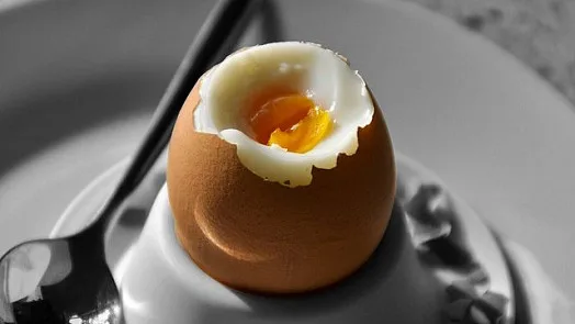 Odloupané vejce v šálku s lžící vedle.