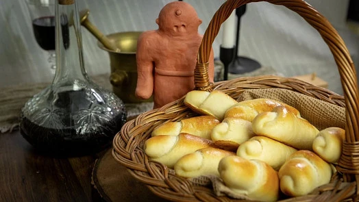 Kos s chlebíčky a lahev vína na dřevěném stole.