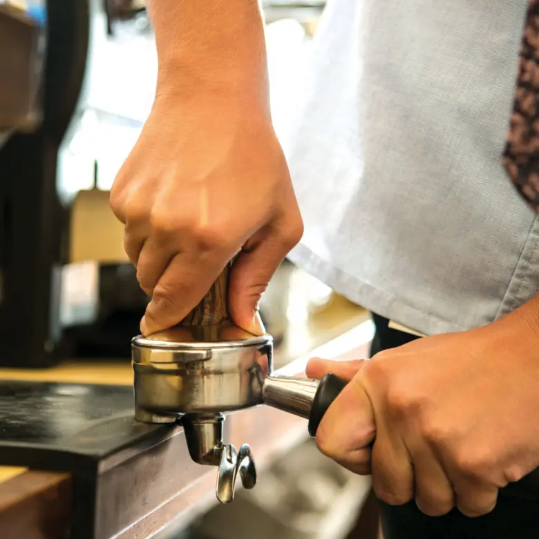 Barista lisuje kávu v portafiltrovu před extrakcí