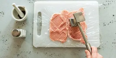 Rozbití kuřecích prsou kladivem na mřížce.