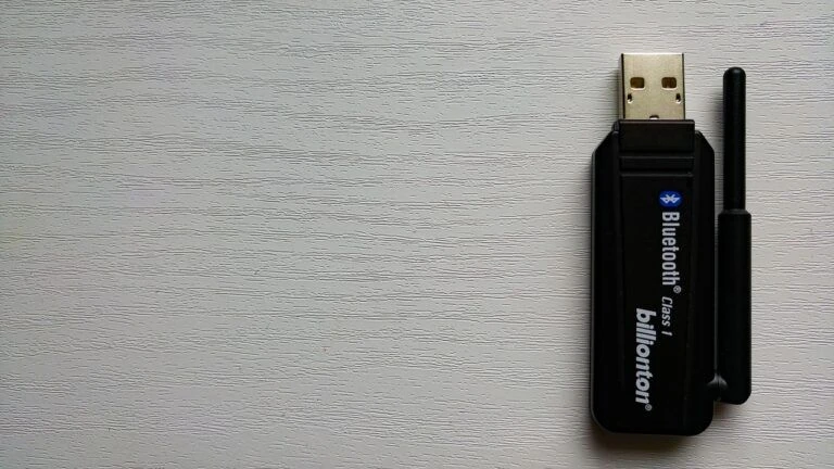 Černý Bluetooth USB adaptér značky Billionton na světlém dřevěném povrchu.