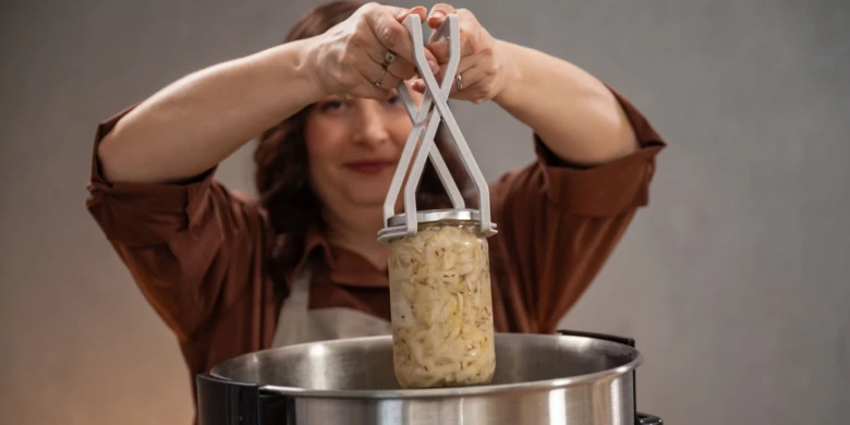Žena zvedá sklenici s konzervovanou potravou pomocí pinzety.
