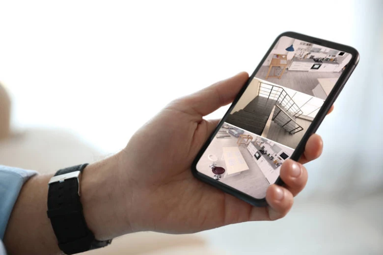 Ruka drží chytrý telefon s videem z bezpečnostní kamery v domě.