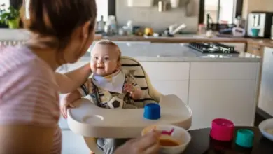 Matka krmit jednoleté dítě v jídelní židli.