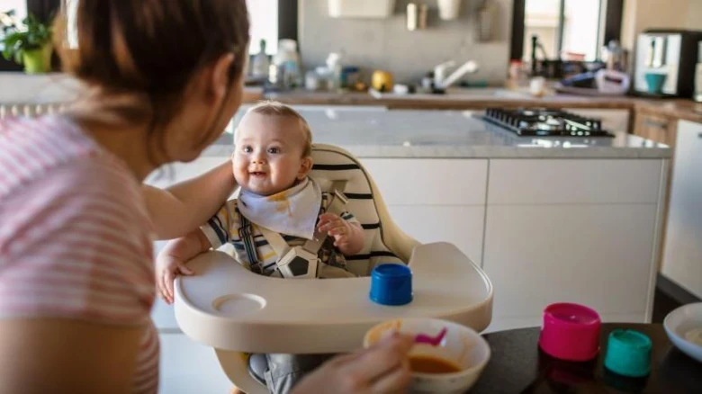Matka krmit jednoleté dítě v jídelní židli.