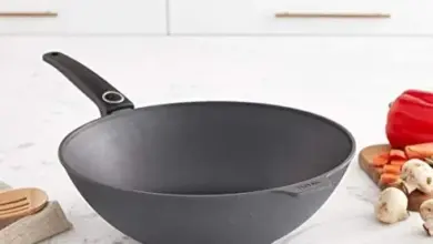 Černá pánev typu wok na kuchyňské desce s čerstvými zeleninovými surovinami.