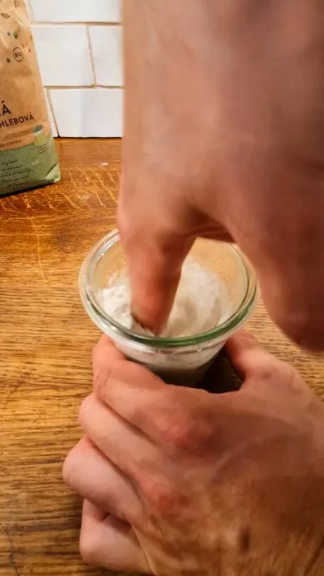 Ruka míchá kvasinky s moukou v malém skleněném kelímku.