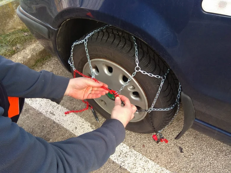 Člověk nasazuje řetězy na pneumatiku automobilu.