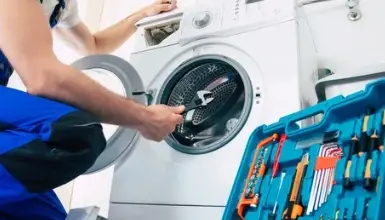 Technik opravuje bílou pračku s otevřeným nádrhem.