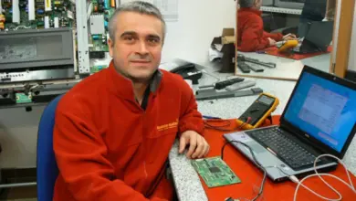 Technik opravující televizi s elektronickými součástkami na stole.