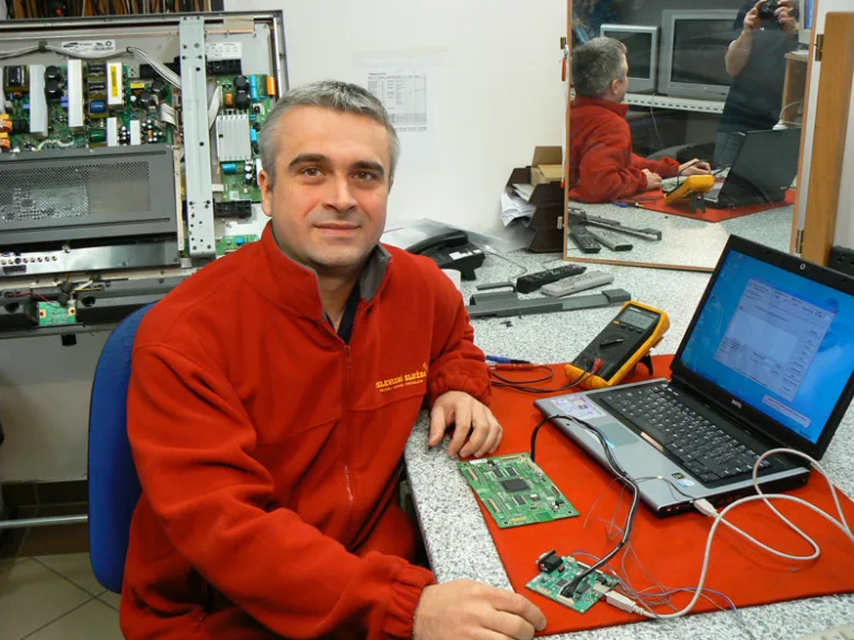 Technik opravující televizi s elektronickými součástkami na stole.
