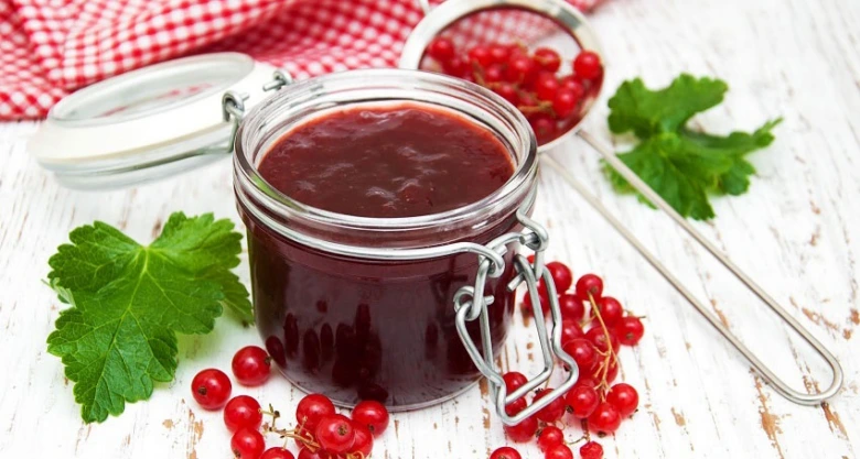 Sklenice angreštové marmelády s čerstvými bobulemi na bílém dřevěném povrchu.