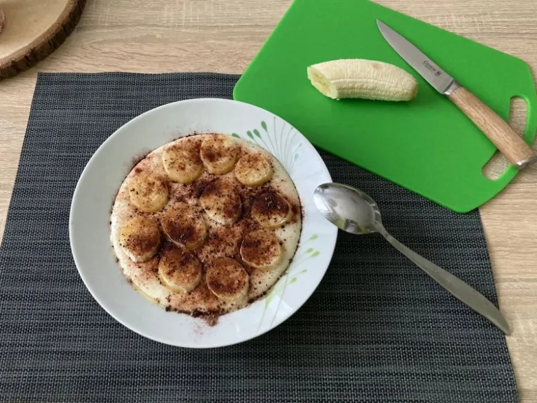 Mísa s nakrájenými banány posypaná skořicí vedle zelené prkénka.