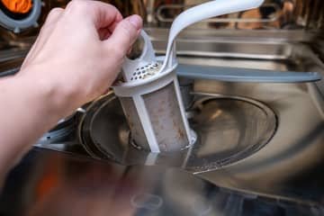 Ruční vyjímání špinavého filtru z myčky nádobí.