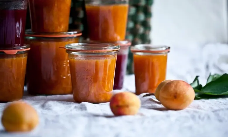Sklenice s marmeládou a čerstvé meruňky na bílém ubrusu.