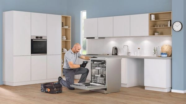Technik opravuje myčku v kuchyni s otevřenou dvířky.