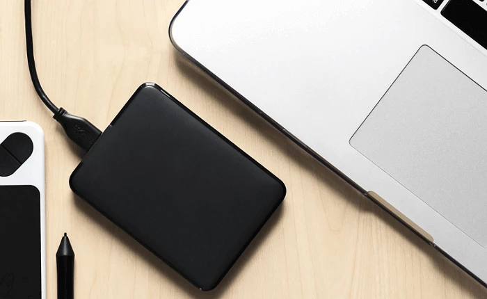 Externí pevný disk připojený k notebooku přes USB kabel na pracovním stole.