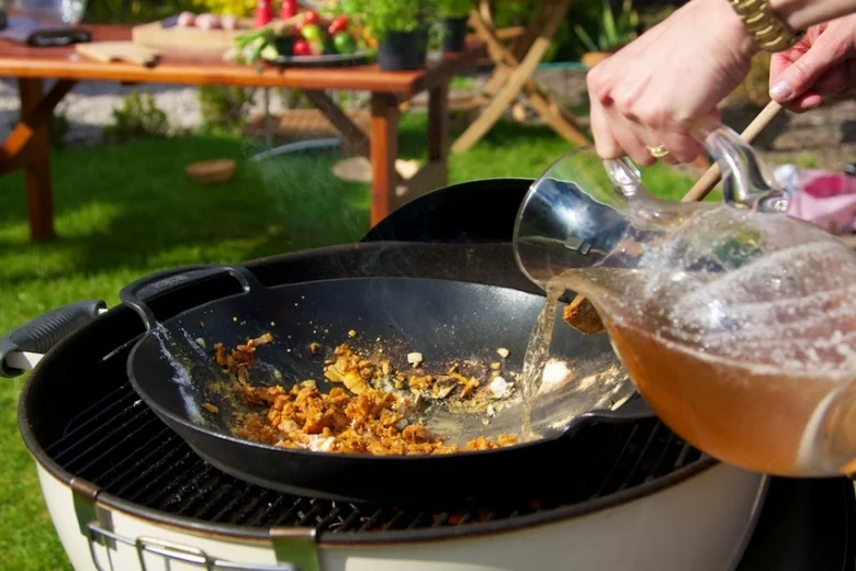 Lidé vaří v woku venku na grilu s přeléváním tekutin.